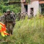 Участники хардбольной игры проходят мимо заброшенного здания с сигнальными флажками.