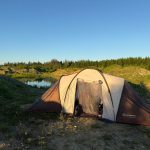Походная палатка у водоёма среди леса и песчаных холмов.