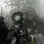 Участник в защитной экипировке целится из оружия сквозь дым или туман.