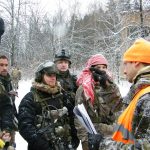 Участники в зимней экипировке стоят среди заснеженных деревьев.